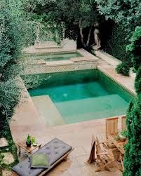 an outdoor swimming pool surrounded by trees and lawn chairs with cushions on the ground next to it