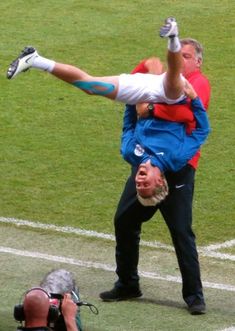 a man on his back holding onto another man's leg as he stands in the middle of a soccer field