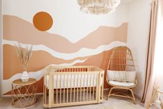 a baby's room with a crib, chair and wall mural