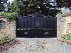 an iron gate in front of a stone wall and brick walkway with trees on either side