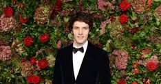 a man in a tuxedo and bow tie standing in front of a floral wall