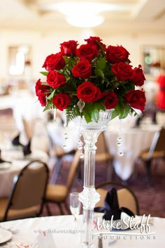 a vase filled with red roses sitting on top of a white tablecloth covered table