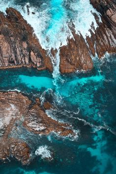 an aerial view of the ocean with rocks and blue water in the foreground, taken from above