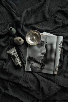 an open book and some glasses on top of a black bed sheet with the image of a woman's face