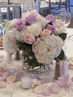 a vase filled with white and pink flowers on top of a table covered in petals