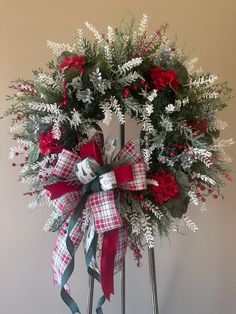 a wreath with red flowers and greenery tied to it on top of a stand