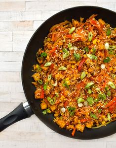 a skillet filled with rice and vegetables on top of a white wooden table next to a black spatula