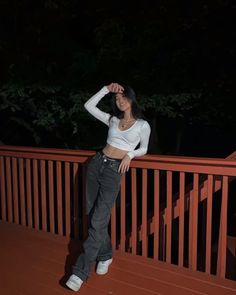 a woman is standing on a deck at night with her hands behind her head and looking off to the side