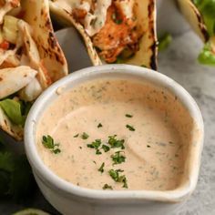 a white bowl filled with sauce next to tortillas and lime wedges on a table