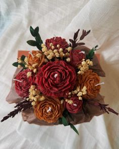 a bouquet of red and orange flowers sitting on top of a white sheet