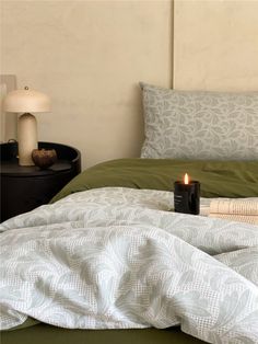 a candle is sitting on the edge of a bed with green sheets and white pillows