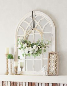 a white mantle with flowers and candles on it, next to an arched window frame