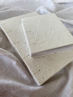 two white notebooks sitting on top of a bed