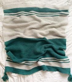 a blanket that is laying on top of a bed with green and white striped blankets