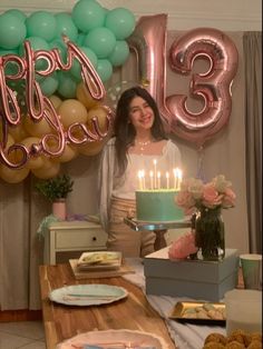 a woman standing in front of a table with a birthday cake and balloons on it