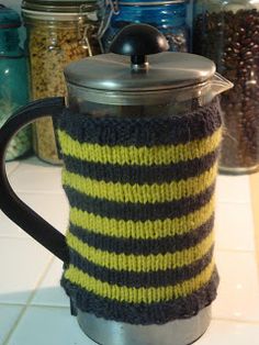 a knitted coffee pot cover sitting on top of a counter next to some jars