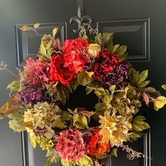 a wreath on the front door with flowers and leaves hanging from it's side