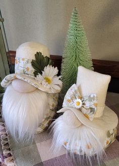 two white hats with flowers on them sitting next to a christmas tree