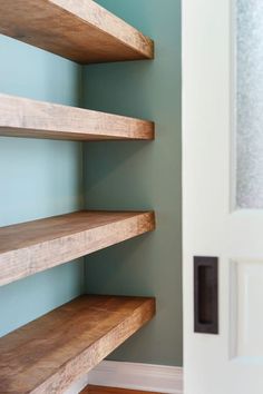 some wooden shelves in the corner of a room next to a white door and blue walls