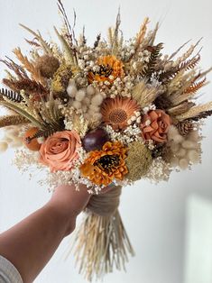 a person holding a bouquet of flowers in their hand with white walls behind them and light colored foliage