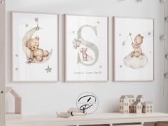 three framed pictures hang on the wall above a white table with toy houses and teddy bears