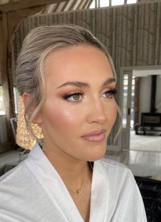 a woman with blonde hair wearing gold earrings and a white shirt is looking at the camera