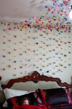 a child laying on a bed in front of a wall with origami birds