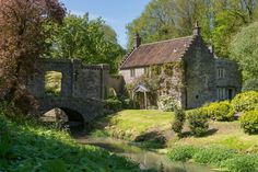 an old stone house with a bridge in the foreground and water running under it