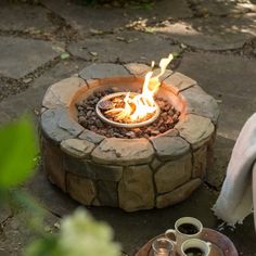 a fire pit sitting on top of a stone slab next to two coffee mugs