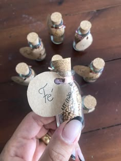 a person holding a tiny bottle with seeds in it next to several small bottles on a wooden table