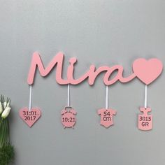 a pink wall hanging with baby's name and birth date on it, next to a vase filled with tulips