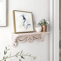 a white shelf with some flowers on it and a framed painting hanging above the shelf