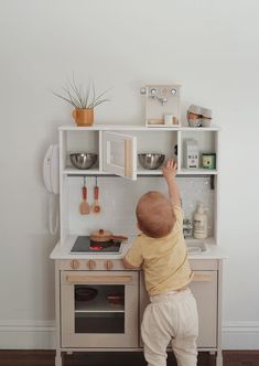 a toddler playing with a toy kitchen set in a playroom or nursery room