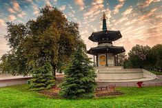 a small pagoda sits in the middle of a grassy area with trees and benches around it