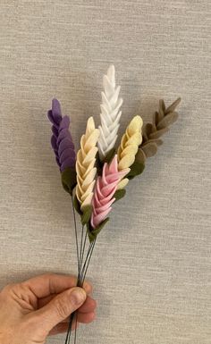 a hand holding some fake flowers on top of a white surface with grey and pink colors