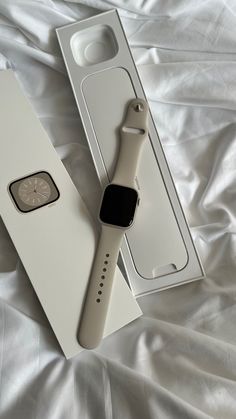 an apple watch in its box on a white bed with the cover pulled down and it's packaging next to it