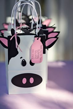 a bag with a cow on it is sitting on a purple table cloth and has tags attached to the handles