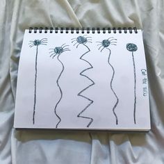 a spiral notebook with drawings on it sitting on top of a white sheet covered bed