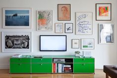 a television is mounted on the wall above a green cabinet with many pictures and books