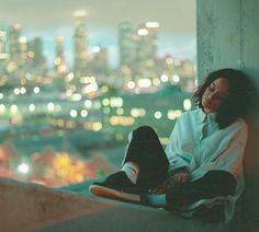 a woman sitting on top of a cement wall next to a cityscape at night