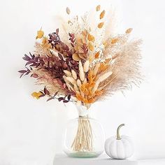 a vase filled with dried flowers next to a white pumpkin