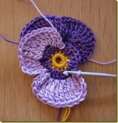 a crocheted flower on a wooden surface with yarn and thread in it, ready to be sewn