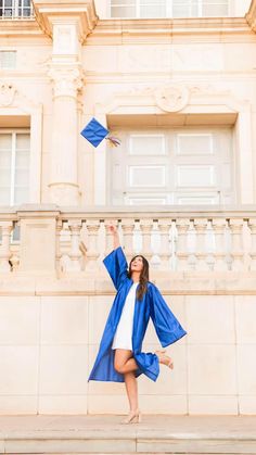 a woman in blue graduation gown and cap jumping up into the air