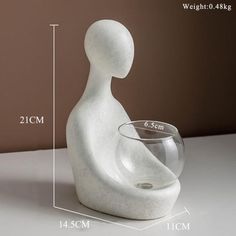 a glass bowl sitting on top of a table next to a white statue that is shaped like a person