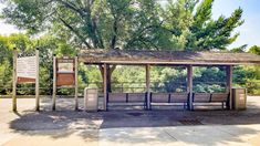 a wooden bench sitting in front of a covered area next to a sign and trees