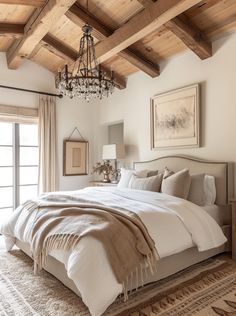 a large bed sitting under a chandelier in a bedroom next to a window