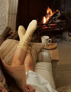 a woman laying in a chair next to a fireplace with her feet up on a pillow