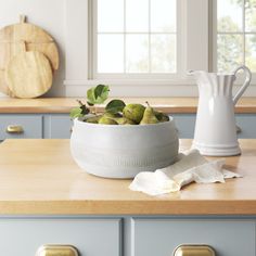 a white pitcher sitting on top of a kitchen counter next to a bowl filled with fruit