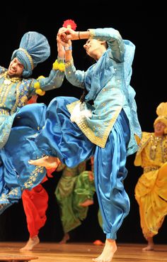 two women in blue and yellow outfits dancing on stage with other people behind them wearing head coverings