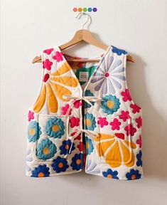 a colorful vest hanging on a wall next to a hanger with an orange and blue flowered design